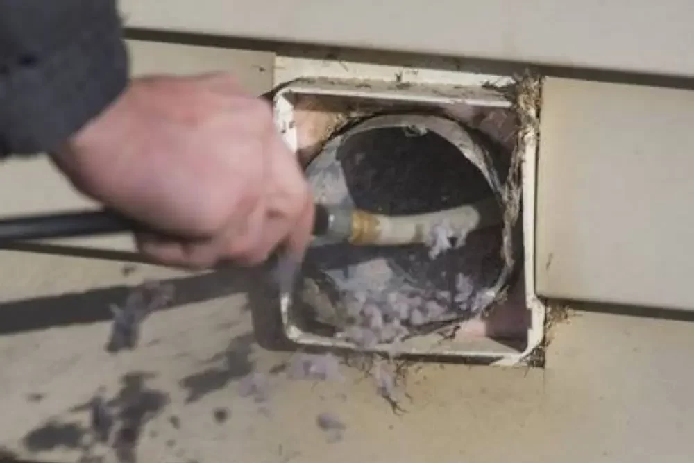 A professional technician cleaning a clogged dryer vent to improve airflow and prevent fire hazards.